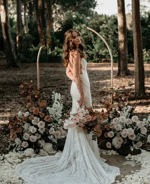 a beautiful bride on her wedding day posing for photographs surrounded by flowers in the outdoor wedding space at gabbinbar