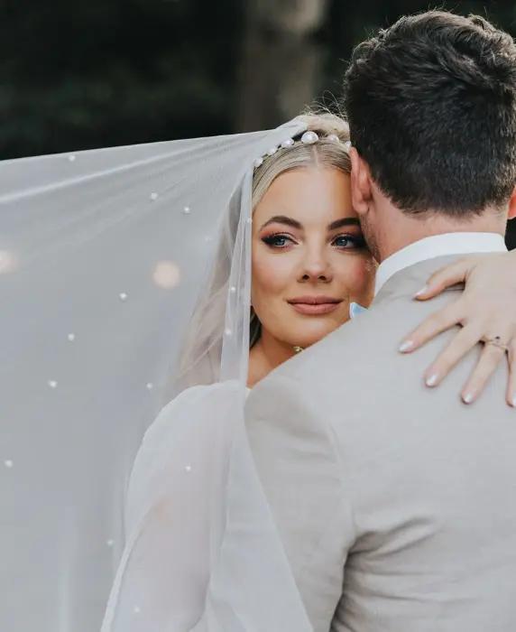 Couple embrace as bride looks over grooms shoulder