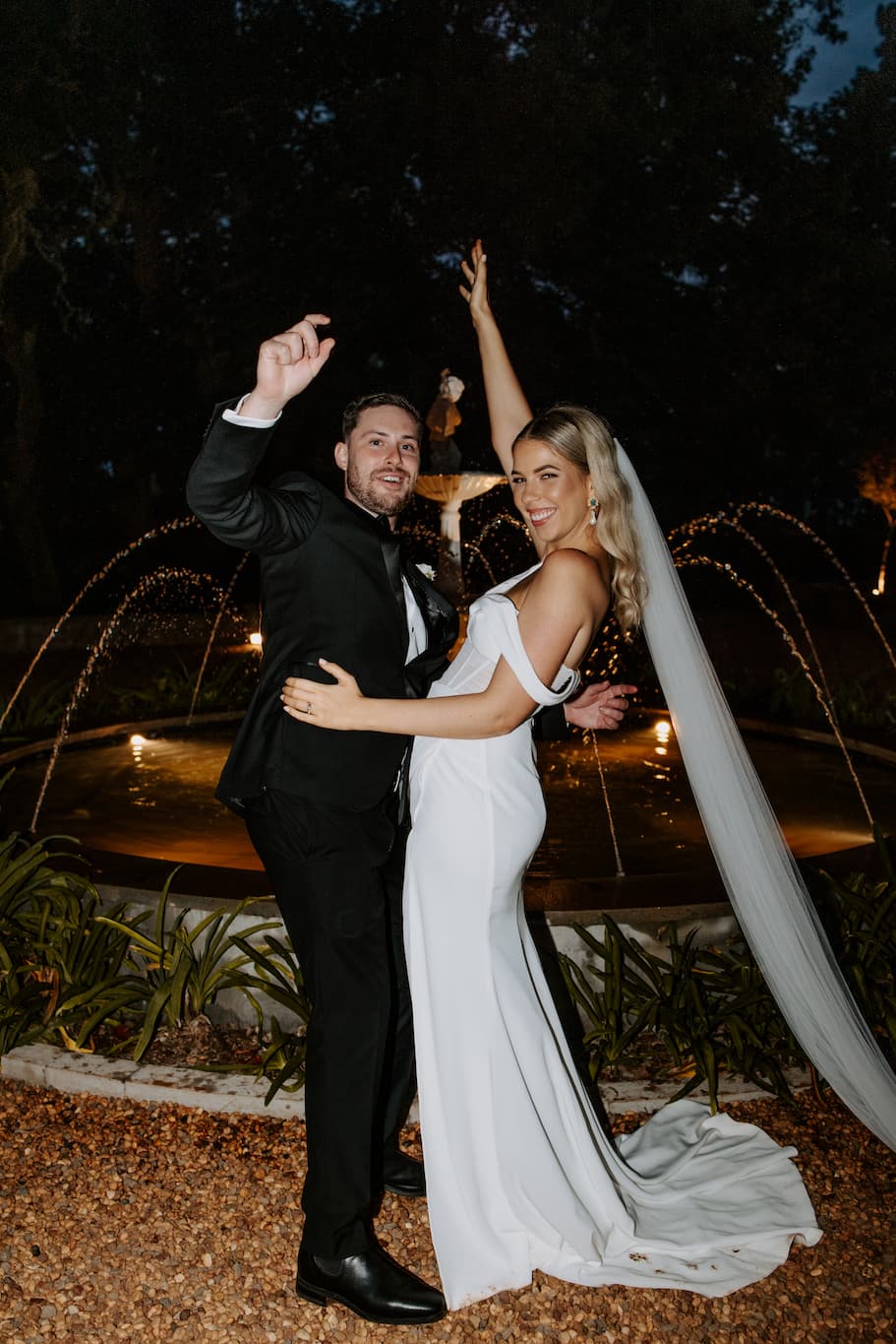 Bride and groom standing in front of fountain dancing