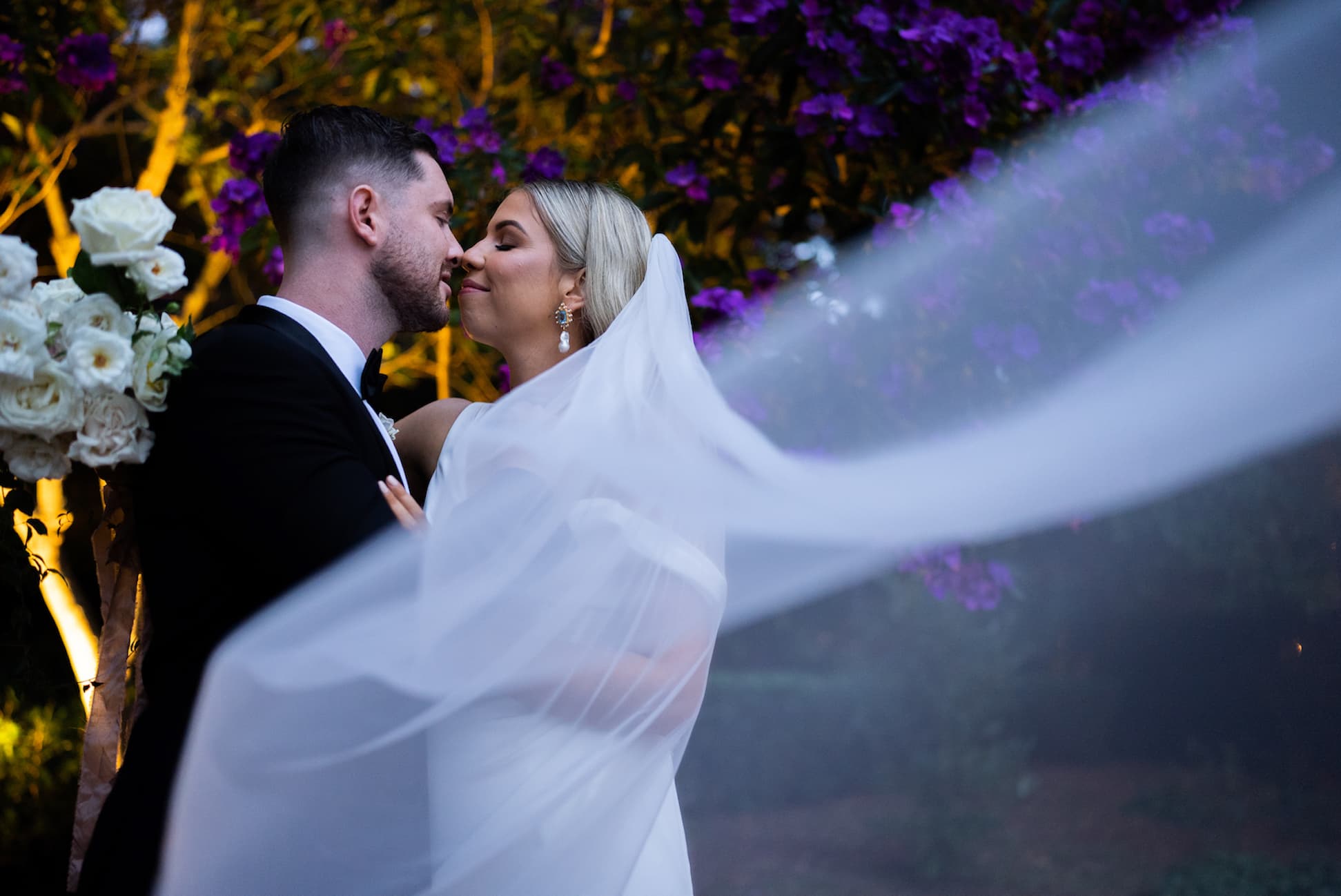 Bride and groom embracing with veil blowing in wind