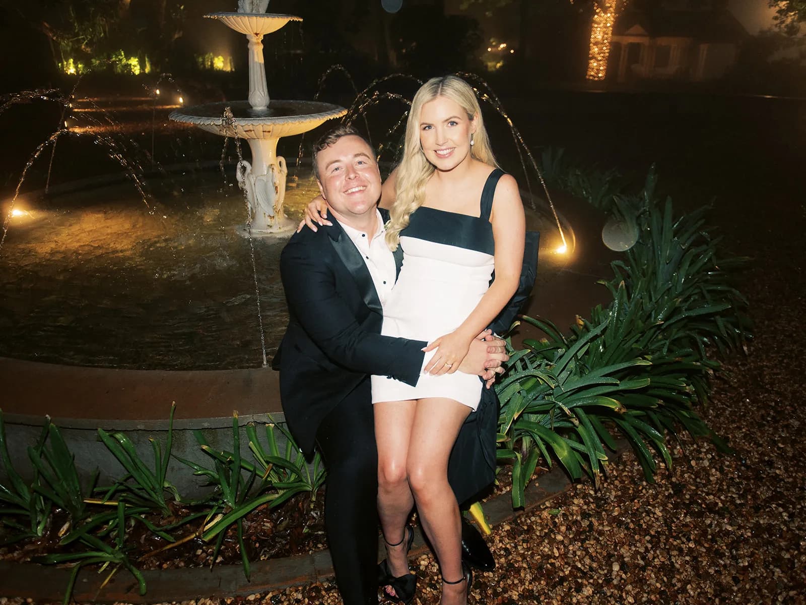 Bride sitting on grooms lap in front of fountain