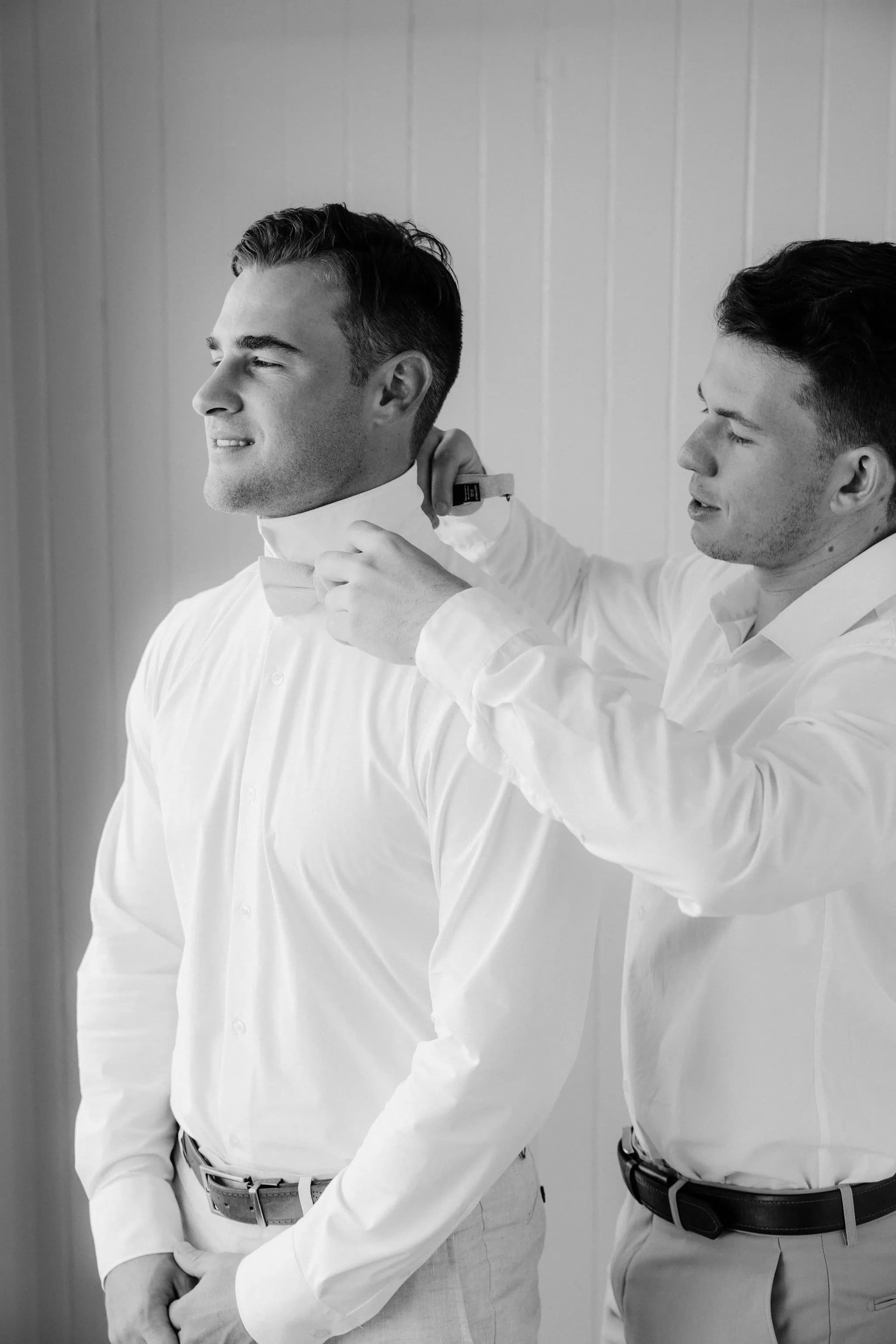 Groom putting on bowtie with groomsmen