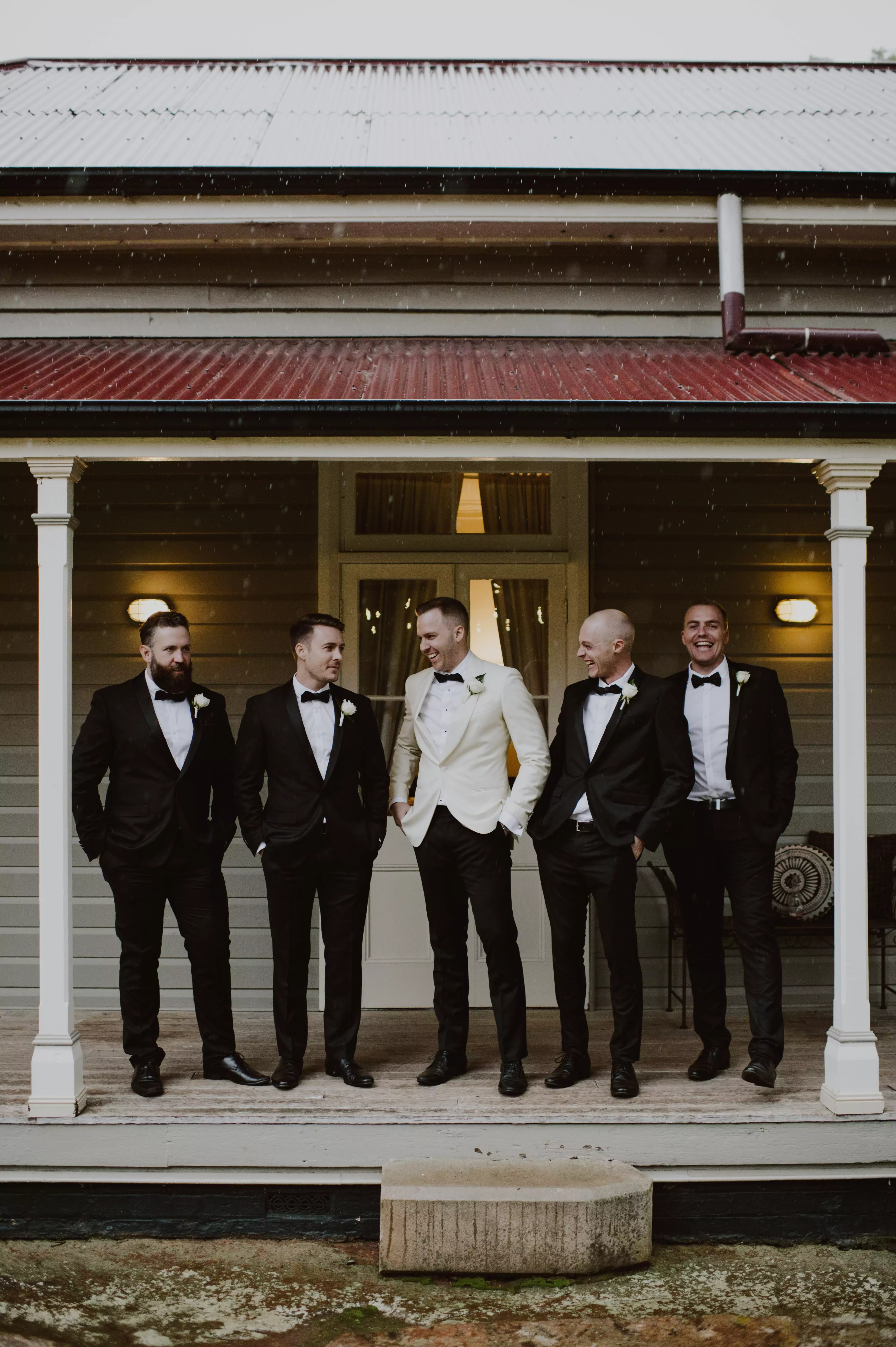 Groomsmen and groom stand under shelter in the rain