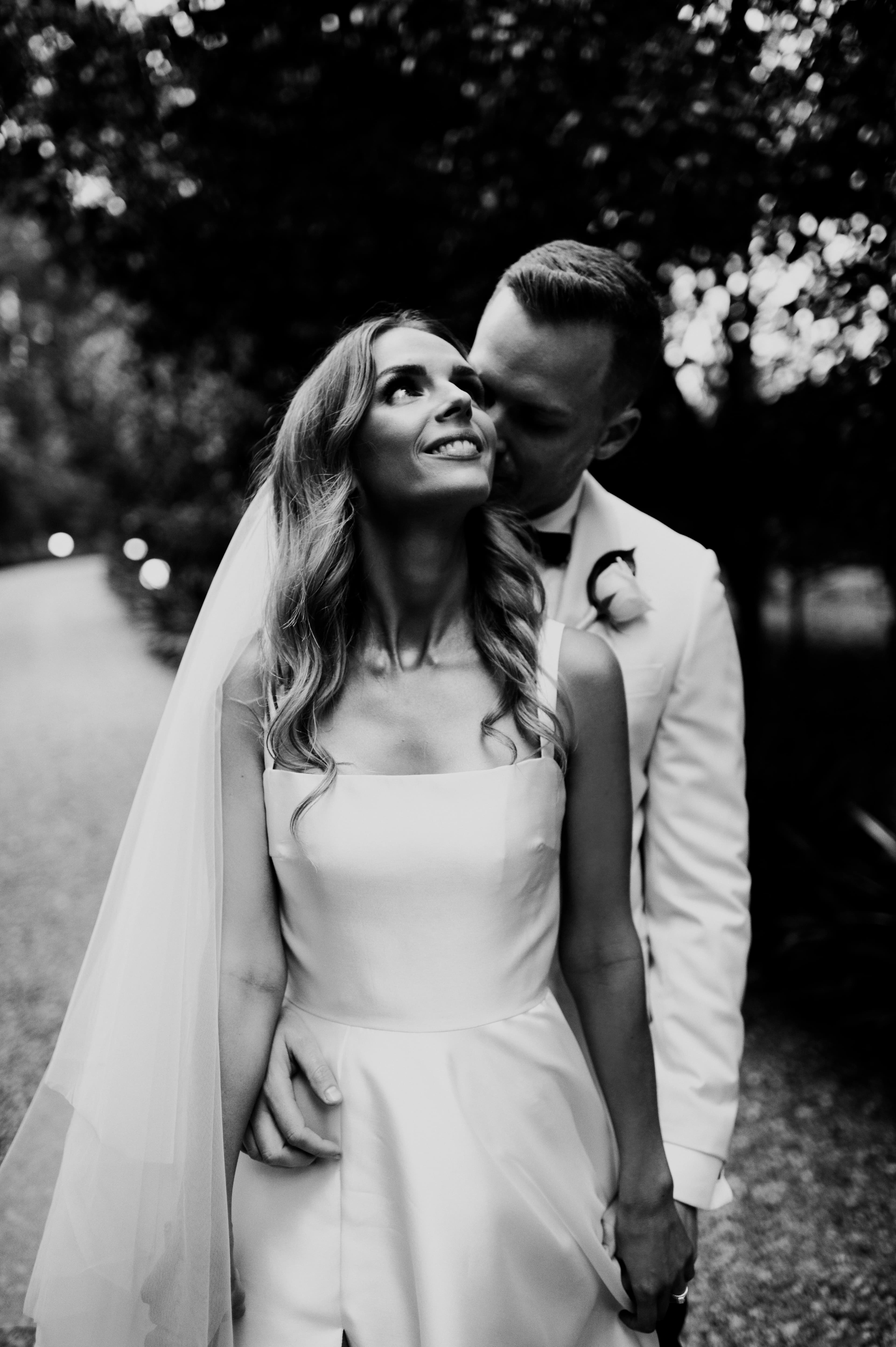 couple pose in black and white photo, bride smiles at the sky