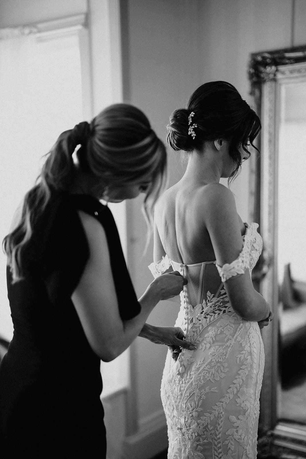 Bridesmaid doing up bride's wedding dress