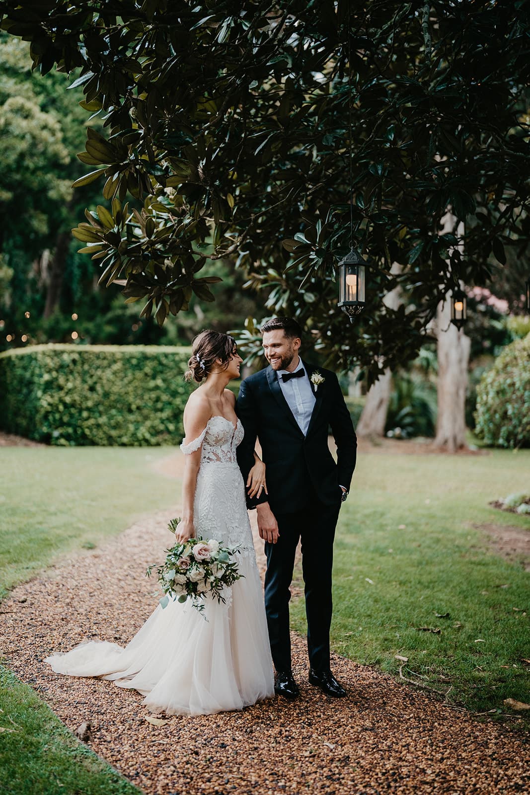 Bride and groom standing under tree with lanterns
