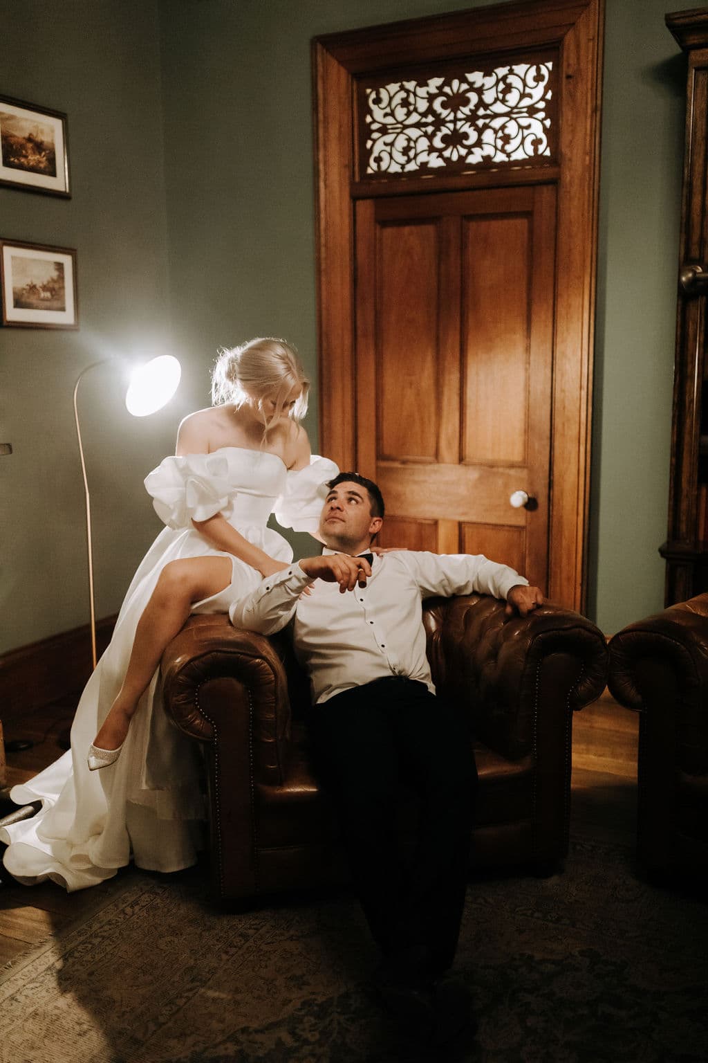 a bride and groom posing for a photograph sitting together on a comfortable leather armchair