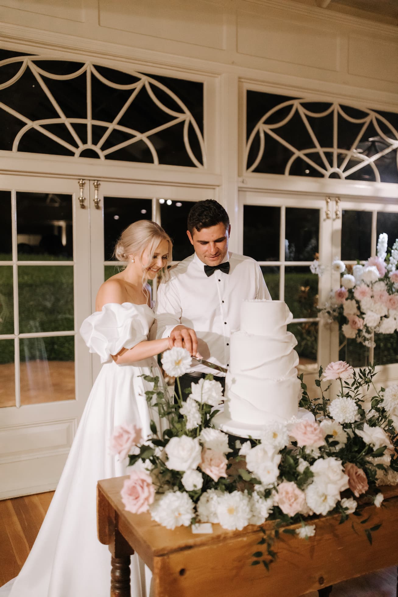 the bride and groom on their wedding day cutting a big white wedding cake surrounded by beautiful flowers