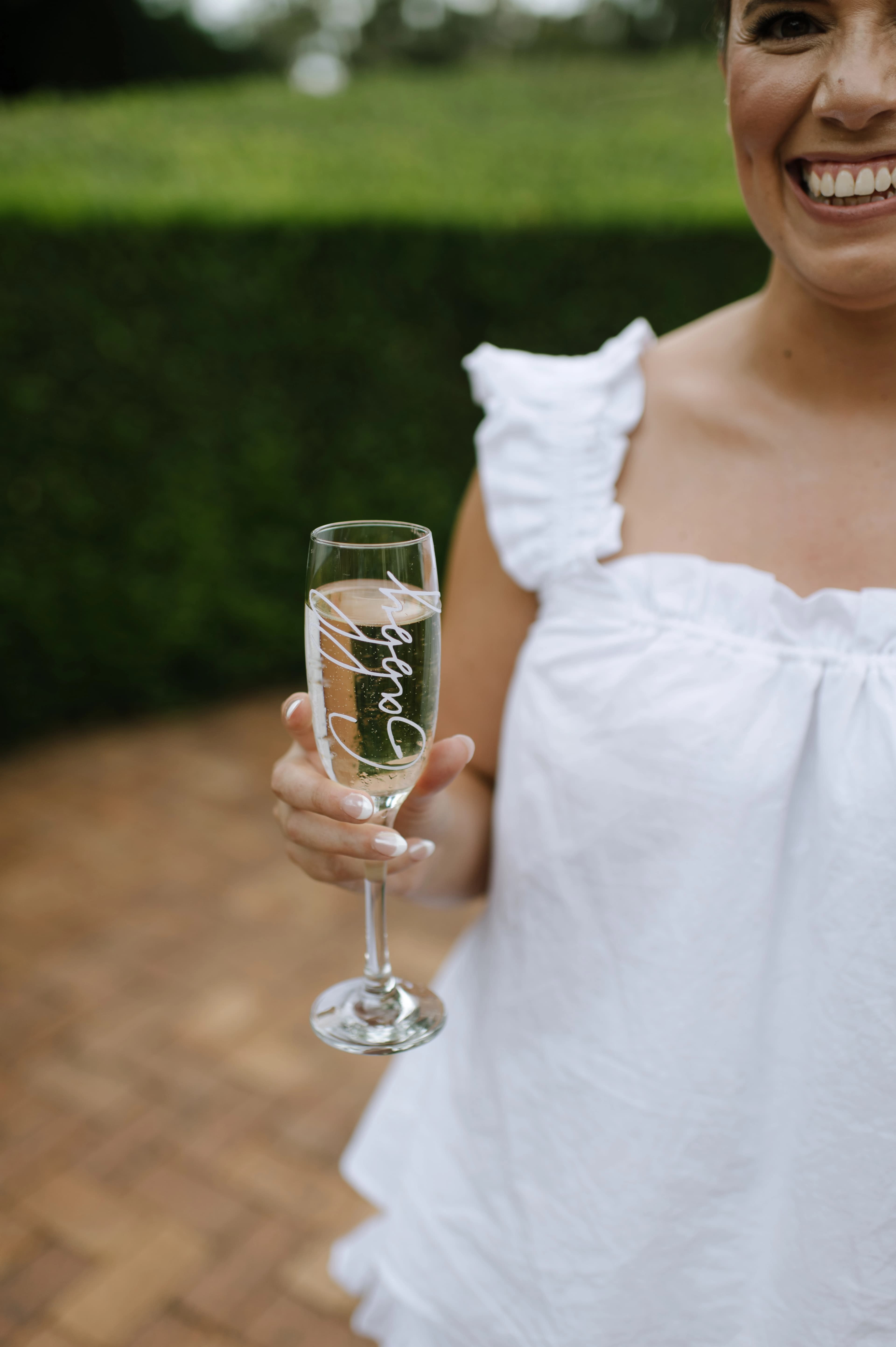 A woman with a joyful expression in a white dress, holding a glass of champagne