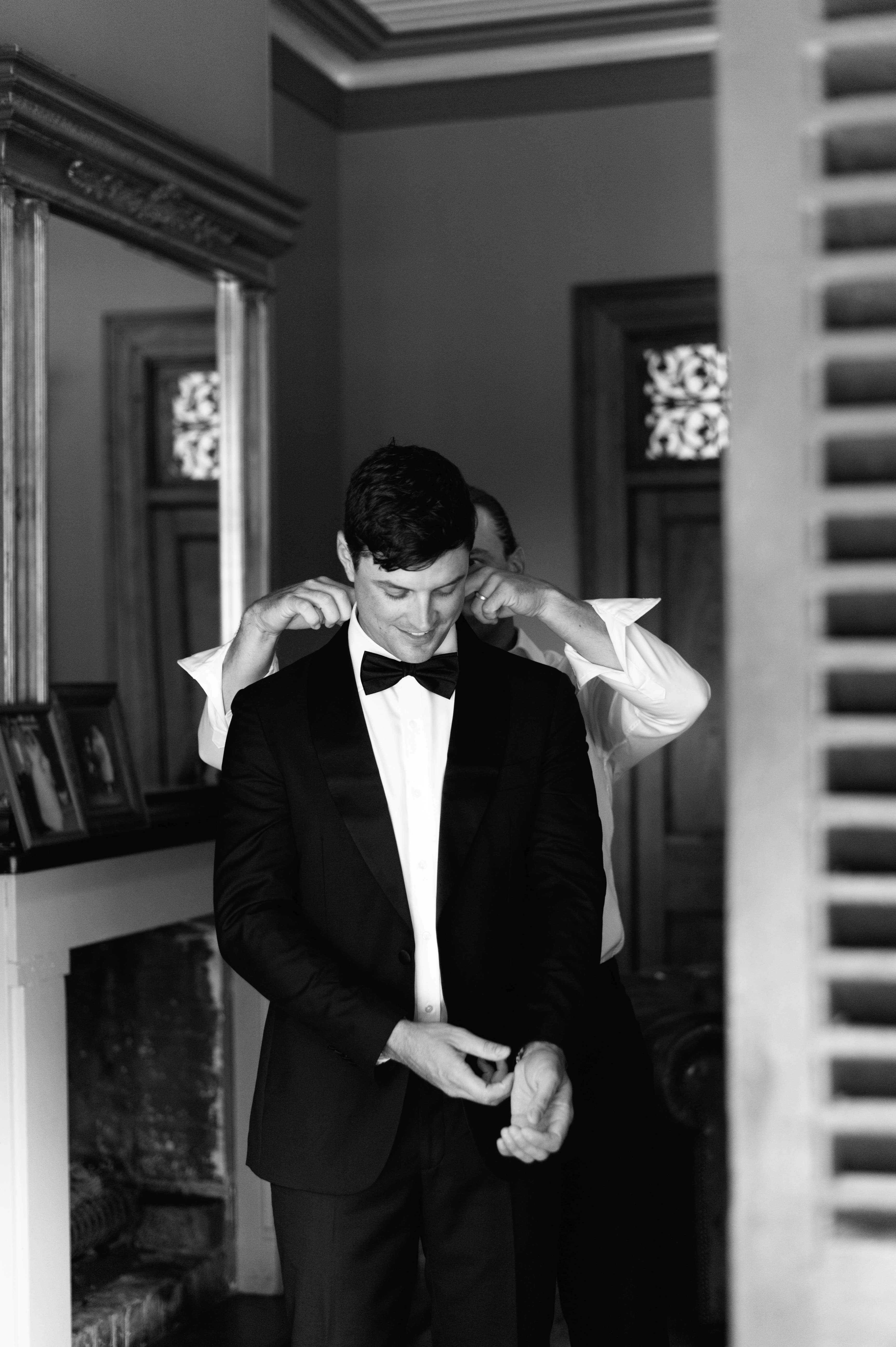 A black and white photo of a man elegantly dressed in a tuxedo, preparing for wedding