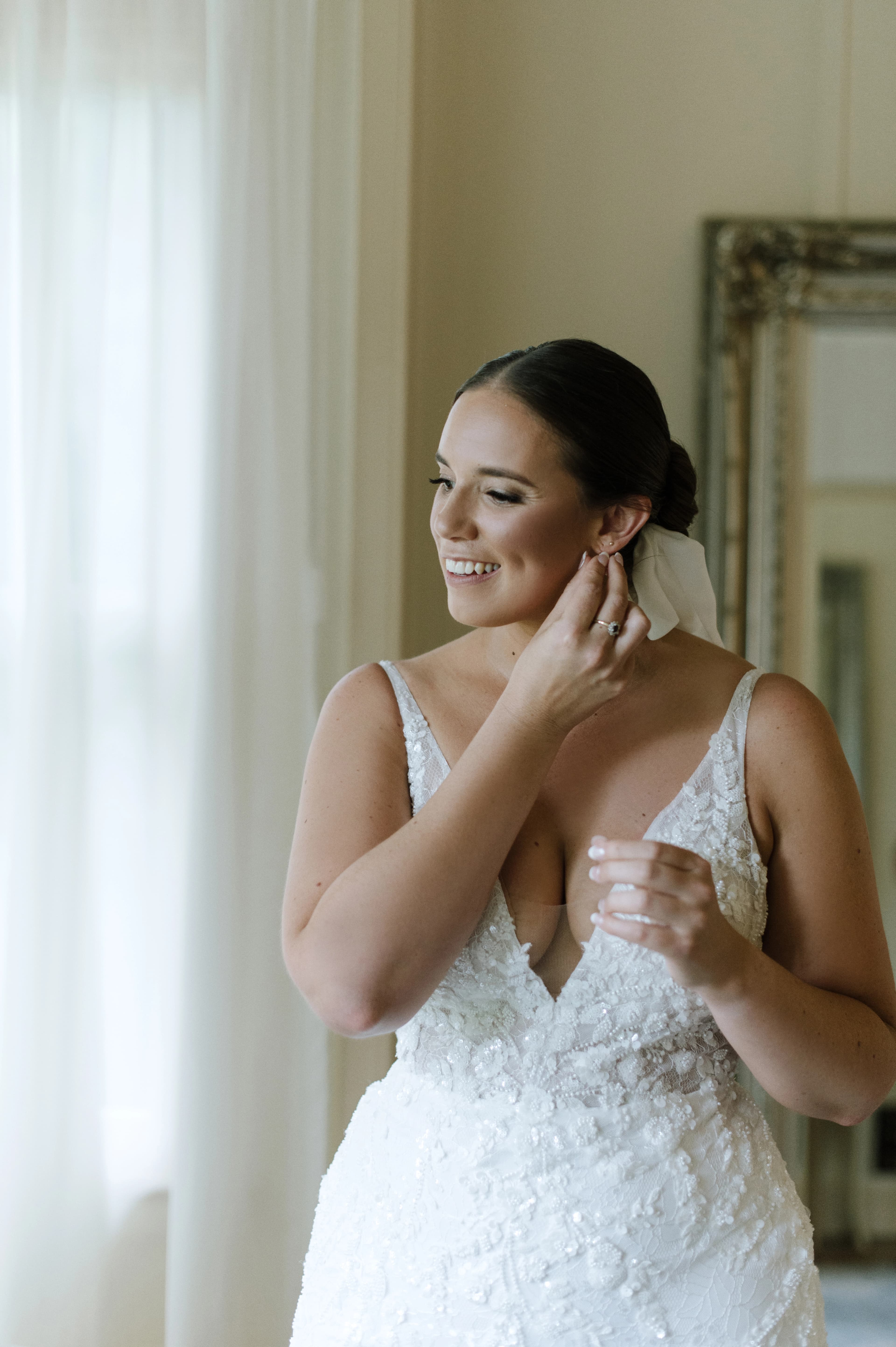 Bride smiling in wedding dress putting earrings in