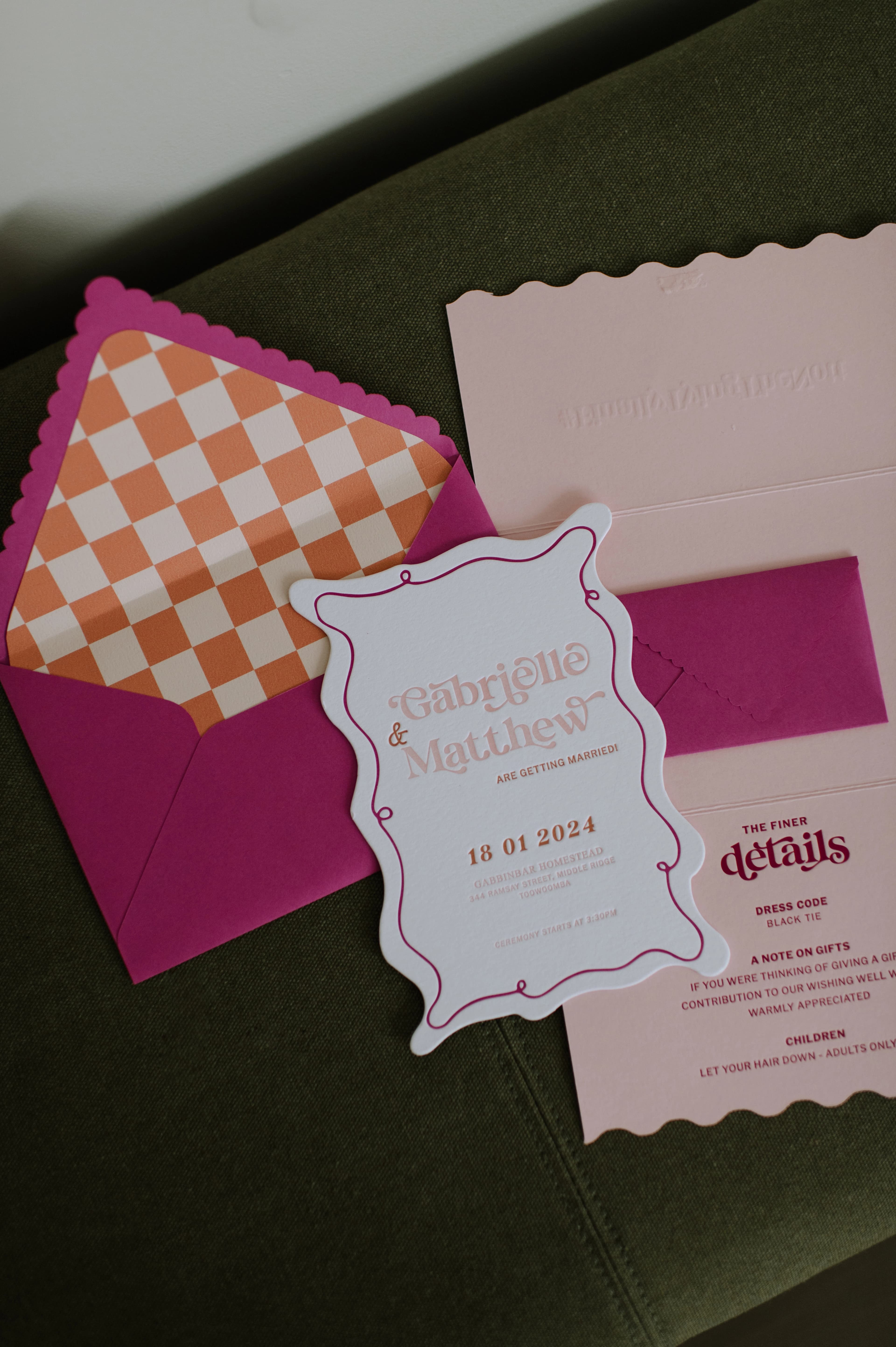 A pink envelope alongside an invitation placed on a green couch.